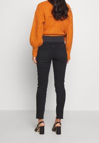 Pull court tricoté orange avec manches bouffantes, associé à un jean skinny noir taille haute. Des sandales à talons noires complètent la tenue.