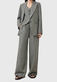 Světle šedý lněný oblek skládající se z blejzru ostrými klopami, vypasované vesty s knoflíky a širokých kalhot; nošeno s černými sandály.