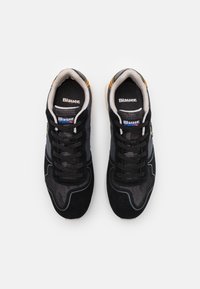Schwarze Sportschuhe mit Netzeinsätzen, Wildlederakzenten und schwarzen Schnürsenkeln. Gold- und Silbertöne am Fersenbereich. Logo auf der Zunge sichtbar.