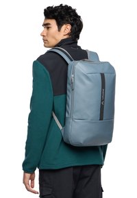 Sac à dos bleu clair au design épuré, fabriqué en matériau lisse, avec une bande noire verticale et des bretelles grises.