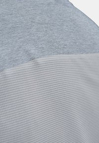 Nærbillede af lyst gråt stof med et tekstureret, gitterlignende mønster under en glat, meleret grå sektion.