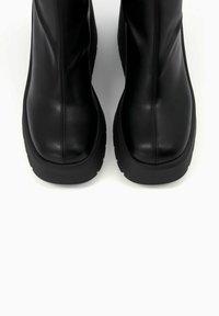 Botines de cuero negro con textura lisa, con punta redondeada y suela gruesa negra. Detalles de costuras en los lados.