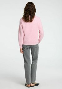 Pull en tricot rose clair avec un col rond et des manches longues, associé à un jean gris droit et des chaussures noires à enfiler.