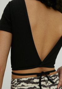 Schwarzes geripptes Crop-Top mit tiefem V-Ausschnitt im Rücken, verziert mit einem gebundenen Detail an der Taille, kombiniert mit gemusterten hochtaillierten Unterteilen.