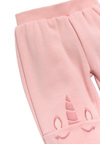 Pantalones de chándal rosa claro con cintura acanalada, que presentan un diseño de unicornio en relieve con cuerno, orejas y detalles de sonrisa cerca de los puños.