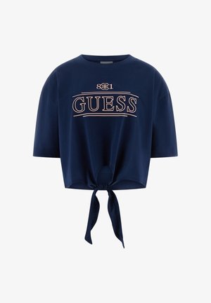 T-shirt court bleu marine à manches courtes, avec un nœud à l'avant et le mot "GUESS" en lettres rose clair sur la poitrine.