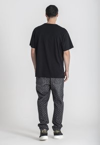 Camiseta negra de manga corta, combinada con unos vaqueros grises de corte amplio y estampado, y zapatillas negras con detalles dorados. Detalle visible en la parte trasera del conjunto.