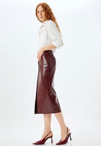 Burgundy imiteret læder midi nederdel med krokodillemønster, sideslids og højhælede slingback-sko sammen med en hvid skjorte.