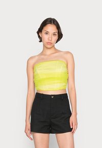 Top cropped sem alças em verde limão brilhante com textura gathered, combinado com calções pretos de cintura alta com fecho de botão e bolsos laterais.