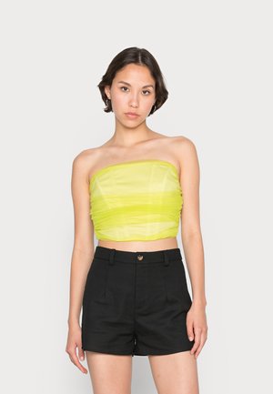 Top cropped sem alças em verde limão brilhante com textura gathered, combinado com calções pretos de cintura alta com fecho de botão e bolsos laterais.