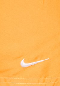 Ryškiai oranžinės Nike šortai pagaminti iš švelnios medžiagos, ant jų siuvinėtas baltas Swoosh logotipas. Medžiaga yra lygi, matomos siuvimo detalės.