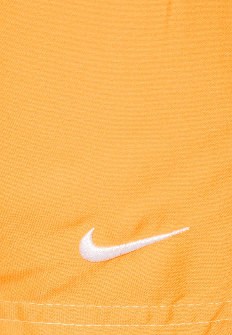 Szorty Nike w jaskrawym pomarańczowym materiale z białym haftowanym logo Swoosh. Tekstura jest gładka z widocznymi detalami szwów.