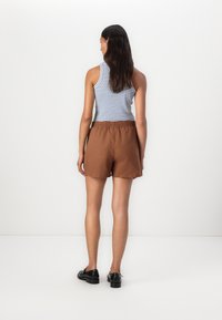 Brune vevde shorts med elastisk midjebånd, kombinert med en stripete ermeløs topp. Har en avslappet passform og jevn tekstur.