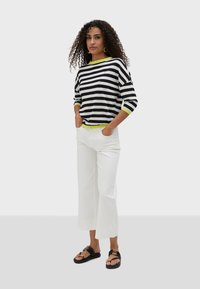 Black and white striped knit top with a bright green neckline, paired with white wide-leg pants and black sandals with gold accents.