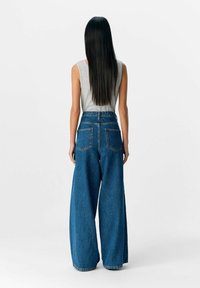 Lichtgrijs mouwloos topje en blauwe wijde jeans met een hoge taille, voorzien van twee achterzakken en een denimtextuur.