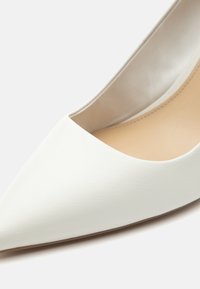 Chaussure à talon haut blanche à bout pointu avec une finition mate lisse et une doublure intérieure beige.