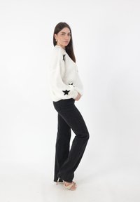 Witte gebreide trui met zwarte sterpatronen, gecombineerd met hoge zwarte flared jeans en lichte sandalen met hakken en bandjes.
