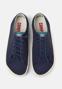 Marineblauwe canvas sneakers met zes gaatjes, platte marineblauwe veters, witte rubberen zolen en rode "Camper" branding op de tong.