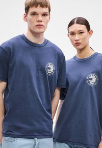 Tamsiai mėlynos medvilninės marškinėliai trumpomis rankovėmis, apvalia iškirpte ir priekyje esančiais logotipais su apskritu dizainu ir tekstu.