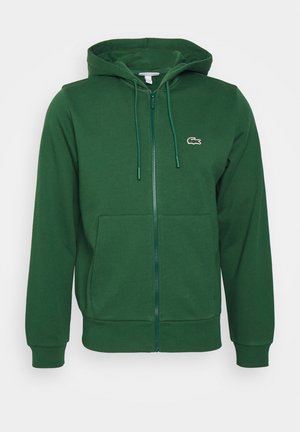 Manche et poche de sweat-shirt vert foncé avec poignets et ourlet côtelés sur fond blanc.