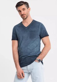 T-shirt blu navy con scollatura a V e finitura testurizzata, maniche corte e taschino sul petto sinistro. Abbinato a jeans in denim chiaro.