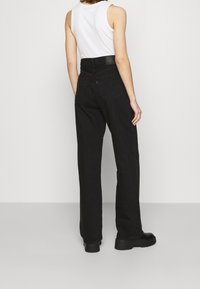 Jeans de mezclilla negros de talle alto con un corte recto. Presentan una cinturilla texturizada y bolsillos traseros. Se combinan con una camiseta sin mangas blanca y botas.