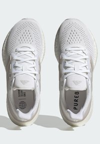 Witte sport schoenen hebben een ademend mesh bovenwerk, veters, een brede tussenzool en een gewatteerde rubberen loopzool, met bedrukte branding aan de binnenkant en aan de zijkant.