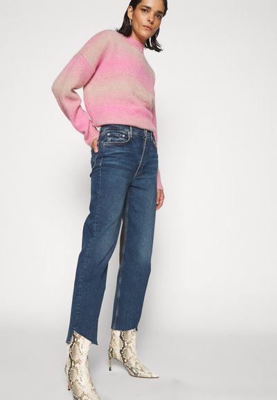 Maglione a maglia con gradiente rosa e crema, abbinato a jeans in denim a vita alta blu con taglio dritto e spacchi laterali, e stivaletti alla caviglia con stampa serpente.