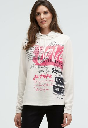 Hooded sweatshirt in light cream with pink and black text. Features a striped pattern and a relaxed fit. Drawstrings at the neckline.