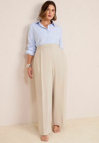 Chemise à rayures bleu clair et blanche avec des manches retroussées, assortie à un pantalon large beige taille haute. Texture de tissu lisse.