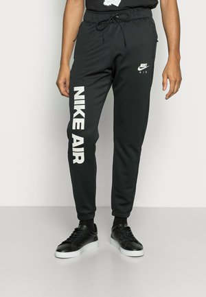 Černé tepláky s tkaničkovým pasem, zúženými nohavicemi a bílým potiskem "NIKE AIR" na boku. Nosené s černými teniskami.