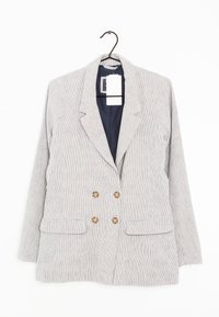 Jasnoszary dwurzędowy żakiet w paski z czterema brązowymi guzikami i kieszeniami z klapami wiszący na czarnym wieszaku.