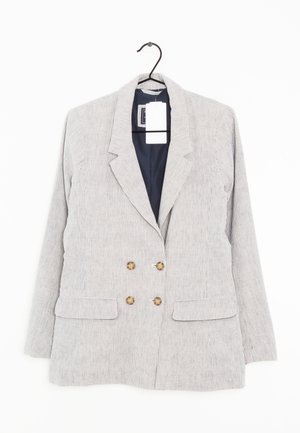 Jasnoszary dwurzędowy żakiet w paski z czterema brązowymi guzikami i kieszeniami z klapami wiszący na czarnym wieszaku.