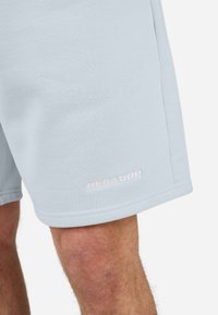 Lyseblå træningsshorts lavet af blødt materiale, med en glat tekstur og hvid "PEGADOR" logo i bunden.