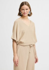 Haut tricot léger beige avec un décolleté en V, des manches courtes et une coupe décontractée. Associé à un pantalon taille haute beige avec une ceinture à nouer.