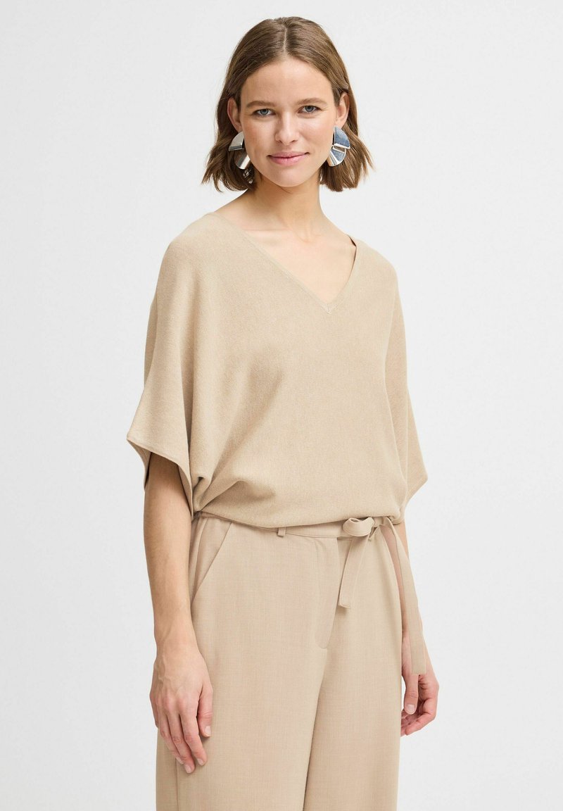 Haut tricot léger beige avec un décolleté en V, des manches courtes et une coupe décontractée. Associé à un pantalon taille haute beige avec une ceinture à nouer.