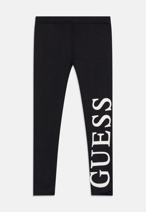 Schwarze Leggings mit großem weißem vertikalem "GUESS"-Logo, das auf dem rechten Bein aufgedruckt ist.
