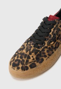 Baskets à imprimé léopard avec une tige en cuir suédé brun texturé, des lacets noirs et une épaisse semelle en caoutchouc naturel. Accents en cuir suédé rouge près de la languette.