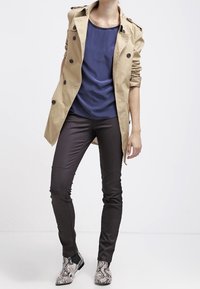 Beige trenchcoat, marinblå topp, svarta figursydda byxor och texturerade ankle boots i ormskinnsprint. Har knappar och axelpartier.