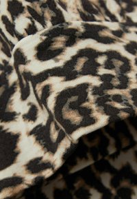 Leopardenmusterstoff mit einer Kombination aus Beige-, Braun- und Schwarztönen, einer weichen, strukturierten Oberfläche und auffälligen Muster variationen.
