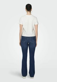 Hvid kortærmet t-shirt og mørkeblå yndlingsjeans, med baglommer og en let tætsiddende pasform. Enkel, afslappet stil.