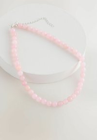 Pink bead necklace made of smooth spheres, featuring a silver clasp and extension chain. Displayed on a circular white surface.