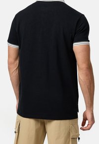 Schwarzes Poloshirt mit einem Kragen und Ärmelbündchen in Weiß gestreift, aus glattem Stoff gefertigt. Die Rückansicht zeigt ein einfaches, klares Design.