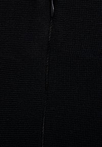 Tessuto nero testurizzato con un fine motivo tessuto, con cuciture visibili lungo una cucitura centrale. Non sono presenti hardware o accenti distintivi.