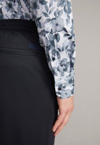 Koszula z długim rękawem w wzory z niebieskim kwiatowym motywem, zestawiona z ciemnymi, gładkimi spodniami z subtelną metką logo na pasku.