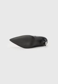 Svarte spisse sko med en blank overflate. Har en teksturert såle og en strømlinjeformet silhuett. Minimalistisk design med subtile dekorasjonsdetaljer.