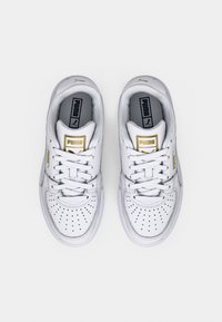 Vita Puma-sneakers med perforerad tåbox, gulddetaljer och grå innersulor. Designade med vita snören och låg profil.