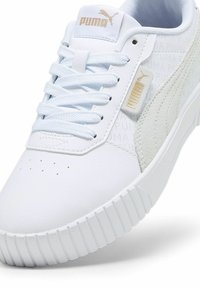 Fehér sneaker sima és texturált anyagokból, kiemelkedő logóval, fűzős dizájnnal és barázdált gumitalppal.