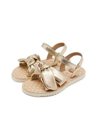 Sandali metallici dorati con grande dettaglio a fiocco, cinturini regolabili e soletta a motivo stellato. Suola in gomma bianca con presa testurizzata.