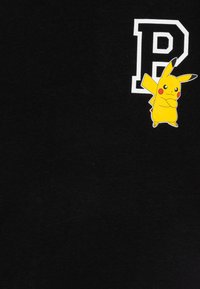 Juodas medvilnės marškinėlis su baltu „P“ grafiku ir spalvinga Pikachu iliustracija kairėje krūtinės pusėje. Minkšta tekstūra, laisvas kirpimas.